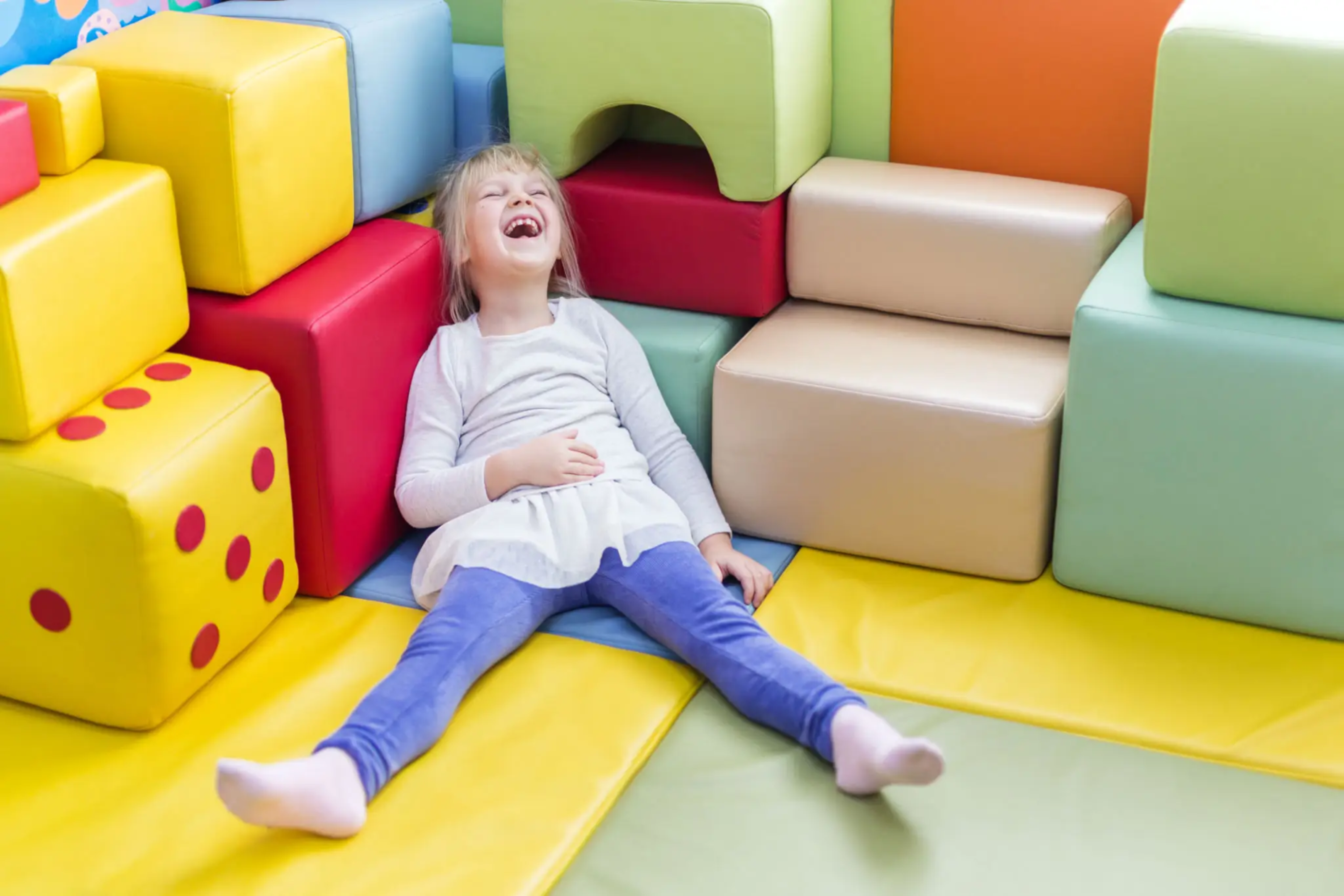 blob-8295fd7 A little girl sitting on the floor of an indoor play area.